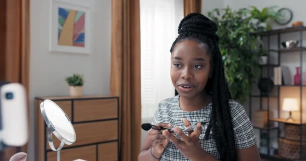 Молодая афроамериканка красотка видеоблогер из дома, создатель онлайн контента, визажистка использует бронзер и подсветку палитры, контуры лица, выделяет щеки — стоковое видео