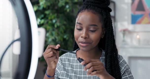 Donna con esperienza nel settore della bellezza gira video sui social media con telefono ad anello. La ragazza applica il mascara, descrive i benefici del prodotto, mostra l'effetto dei fan delle ciglia allungate e ispessite — Video Stock