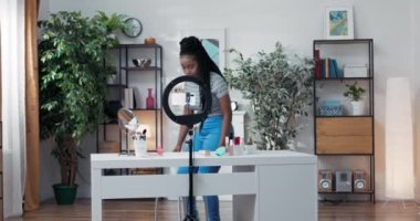 Koyu tenli ve uzun siyah saçlı bir kadın sosyal medya için makyaj videoları hazırlamaya hazırlanarak odaya giriyor. Kozmetik kızı olan beyaz masa takipçilerine el sallayarak halka ışığını ayarlıyor