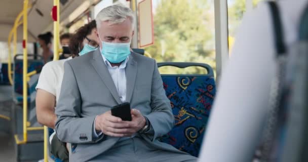 Elegante hombre de traje con pelo gris tiene máscara protectora en paseos por la cara transporte público — Vídeo de stock