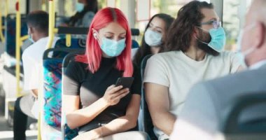 Pembe saçlı, koruyucu maskeli çekici bir kız toplu taşıma otobüsüne biniyor, akıllı telefon kullanıyor.