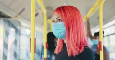 Yüzüne koruyucu maske takmış pembe saçlı bir kadın halka açık bir yere biniyor.