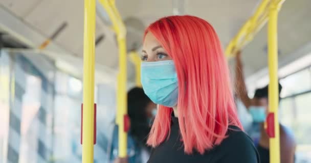 Una mujer con el pelo rosa con una máscara protectora sobre su cara monta un público — Vídeos de Stock