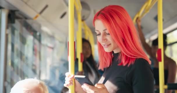 Kaunis hymyilevä tyttö vaaleanpunaisilla hiuksilla ratsastaa bussilla, joka pitää kiinni kaiteesta., — kuvapankkivideo