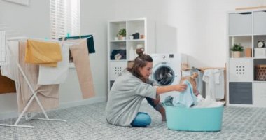 Bir anne ev işleri sırasında kızıyla çamaşır odasında vakit geçirir. Şirin küçük bir kız bir kase elbisenin içinde oturuyor gülümsüyor, kadın tişörtünü çıkarıyor ve çocuğa konuştuklarını gösteriyor.