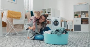 Kadın çamaşır odasında çamaşır katlarken bebek beklenmedik bir şekilde annelerin sırtına atlar. Sevimli, güzel bir kız bebek ona sarılıyor, annesi kollarını bir uçak gibi açıyor.