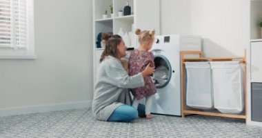 Kadın, küçük çocukla çamaşır odasında, banyoda vakit geçiriyor, doğum iznindeyken ev işlerini yapıyor, kızına bakıyor, çamaşır makinesini nasıl kullanacağını gösteriyor.