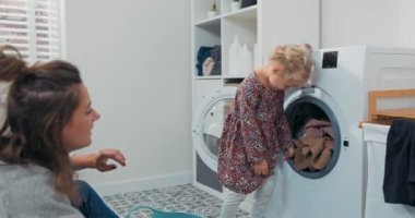 Anne kızıyla banyoda, çamaşır odasında günlük ev işleri yaparken vakit geçirir. Kız çamaşır makinesinden bir şeyler çıkarır ve renkli temiz giysileri kaseye koyan kadına verir.