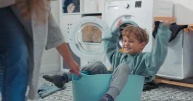 Annesiyle oynayan mutlu oğlanın yakın plan çekimi. Çamaşır kabında oturan çocuk bir kadınla vakit geçirmek ve ev işlerine yardım etmek istiyor. Annesi çocuğu çamaşır odasında sürüklüyor.