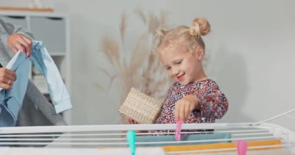 Nettes kleines Mädchen im Badezimmer. Saubere gewaschene Kleidung auf dem Wäscheständer. Mütter helfen, süßes Kind hilft bei der Wäsche, sie hängt Handtücher zum Trocknen und Clips — Stockvideo