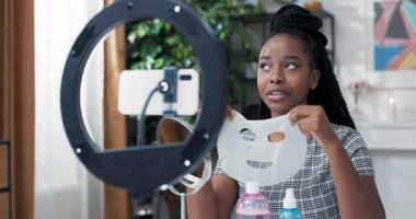 Güzellik blogcusu ya da vlogger ürün değerlendirmesi sosyal medyada paylaşılacak. Kadının elinde yüz bakımı maskesi var. Gözlemcilere bunun faydalarını anlatıyor.