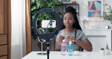 Bir kadın, halka lambası ve telefon kullanarak sosyal medyada bir video kaydediyor. Etkilenen güzellik içeriği yaratır, cilt bakımı hakkında konuşur, gözlemcilere yüz masajı taşı gösterir, gua sha