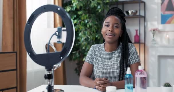 Female influencer sits at desk prepared to record live streaming for social media channel, tripod with ring light and phone in front of her, girl smiles at camera — Stock Video