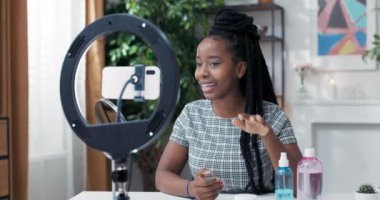 Popüler bir nüfuzlu vlogger, halka ışığı standında kurulmuş bir telefona konuşan sosyal medyada bir video yaratıyor, bir kadının önünde yüz bakım ürünleri var, kameraya bakıyor ve geniş bir şekilde gülümsüyor.