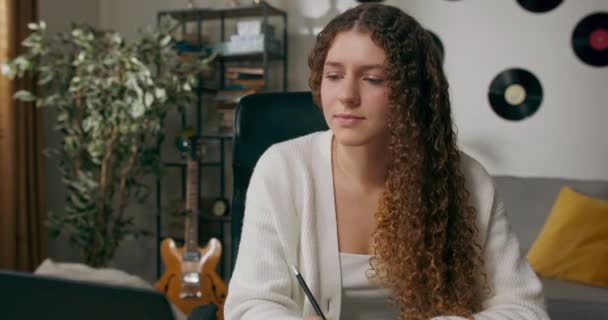 Dziewczyna Kręconymi Włosami Siedzi Przy Biurku Salonie Pracuje Laptopie Robiąc — Wideo stockowe