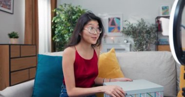 Neşeli genç bayan stilist sosyal medyada vloglar, giyim markası işbirliğinden bir paketi açıyor. Blogcu halka ışığı olan bir telefon kullanıyor..