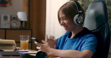 Bir genç ev ödevi yaparken kablosuz kulaklıkla müzik dinler. Genç bir çocuk telefonunda bir çalma listesi arıyor ve şarkıları olan bir uygulama kullanıyor..