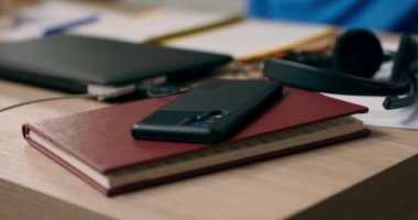 Genç bir çocuk masanın üzerindeki bir kitaba uzanmış telefona uzanıyor. Kablosuz kulaklık takan bir çocuk müzik dinliyor, arkadaşlarına mesaj gönderiyor, sosyal medyada geziniyor ve şarkı listesi çalıyor..