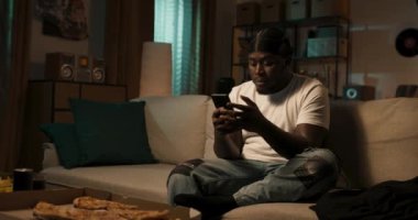 Koyu tenli, beyaz tişörtlü ve siyah bandanalı rahat koltukta elinde cep telefonuyla oturan sakallı adam, kısa mesajlar üzerine üzücü tartışmalar yapıyor..