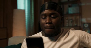 Bir adam elinde akıllı bir telefonla kanepede oturuyor, web sitelerine göz atıyor, telefona uygulamalar yerleştiriyor, elektronik alışveriş listesi yapıyor, hatırlatıcıları clanedar 'a koyuyor..