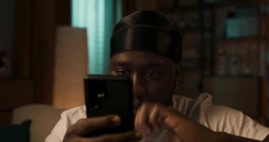 Modern evdeki koltukta otururken telefonu kullanan mutlu sakallı bir iş adamı. Mobil cihazlarda çalışan gençlerin kavramı.