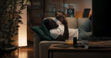 Rahat bir genç adam rahat bir kanepede uzanıyor, hafta sonları boş zamanlarının tadını çıkarıyor, arkadaşlarıyla telefonda sosyal medyada sohbet ediyor, video görüşmesi yapıyor..