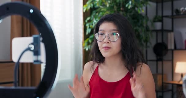 亚洲选美博主正在为观众录制化妆教学视频 通过频道播放 一边挥手站在讲台上 一边点燃戒指 一边看广告 — 图库视频影像