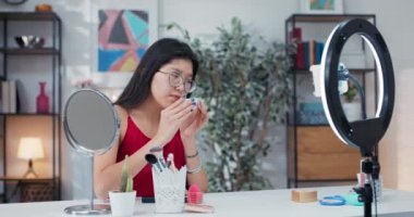 Makyaj sanatçısının sosyal medya izleyicilerinin önünde kozmetik ürününü test ettiği yakın çekim. Kız pirinç tozunu test ediyor ve aynaya bakarken fırçayla yüzüne uyguluyor..