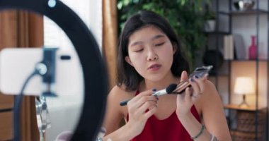 Genç bir Asyalı güzellik, vlogger, çevrimiçi içerik yaratıcısı, ve makyaj sanatçısı, bronzlaştırıcı ve fosforlu kalem paleti kullanır, yüz hatları çizer ve yanakları renklendirir..