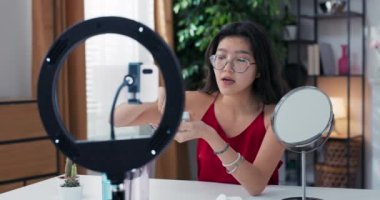 Nüfuzlu blogcu cilt bakımı hakkında konuşuyor. Kadın, yüz yüze nemlendirici sürerken video blogunu telefonla kaydediyor. Bir kız güzellik tedavilerinden bahseder.