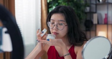 Nüfuzlu blogcu cilt bakımı hakkında konuşuyor. Kadın, yüz yüze nemlendirici sürerken video blogunu telefonla kaydediyor. Bir kız güzellik tedavilerinden bahseder..