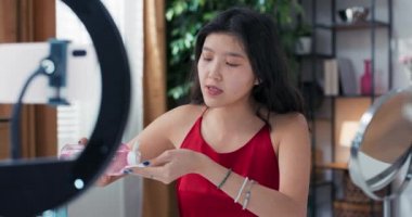 Kadın nüfuzlu biri, temeli pamuk yumaklarıyla nasıl temizleyeceğini ve makyaj çıkarıcıyı nasıl kullanacağını gösterir. Evde canlı yayın için bir video günlüğü kaydetmek için halka ışığı olan bir tripod telefon kullanılır.