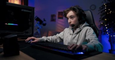 Odaklanmış genç çocuk kulaklıkla bilgisayarın başına oturur, çocuk çok oyunculu nişancı oyunları oynar takım üyeleriyle konuşur, karanlık oda ışıklarıyla aydınlatılır..