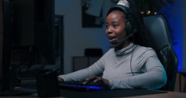 Profesyonel oyuncu genç kız kulaklıkla takımla bilgisayar oyunu oynuyor, sanal şampiyonada turu kazanıyor, seviyeyi geçiyor, kadın zaferden zevk alarak elini kaldırıyor..