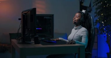 Kadın kulaklıkla konuştuğu takımla profesyonel olarak bilgisayar oynuyor, takım sanal çevrimiçi şampiyonada kazanıyor, arkadaşlarıyla kız şakaları yapıyor, karanlık oda mavi ellerle aydınlatılıyor..