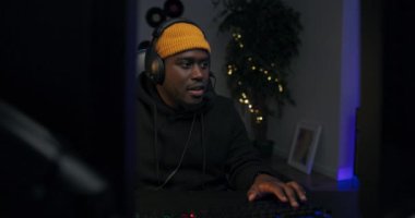 Sweatshirt ve şapka giyen rahat bir adam. Adam monitörün önünde oturuyor, bilgisayar oyununda muzaffer. Zafer sevinci ile ellerini havaya kaldırıyor. Sanal takım üyeleriyle birlikte zafer kazanıyor..