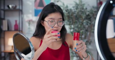 Güzellik modeli makyaj yapıyor. Kız aynaya bakıyor ve temelini pembe süngerle kuruyor. Güzel genç kadın sosyal medyada izleyicilere özel ipuçları kaydediyor..