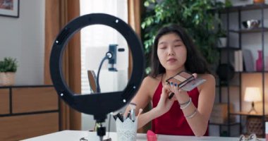 Yüzü fosforlu kalemle şekillendirme talimatları. Asyalı güzel bir kadın sosyal medyada canlı yayın yapıyor. Bir kız hafif bir yüzük kullanıyor ve internette güzellik tavsiyeleri veriyor..