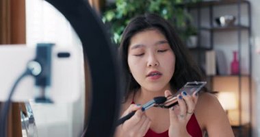Genç bir Asyalı güzellik, vlogger, çevrimiçi içerik yaratıcısı, ve makyaj sanatçısı, bronzlaştırıcı ve fosforlu kalem paleti kullanır, yüz hatları çizer ve yanakları renklendirir..