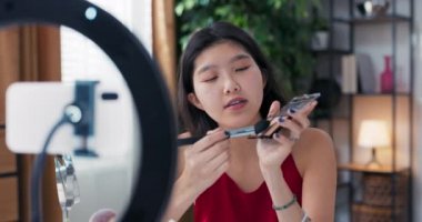 Açık tenli Asyalı kadın profesyonel vlogger ya da blog yazarı sosyal medyada paylaşmak üzere makyaj eğitimi veren bir halka ışığı kaydediyor.