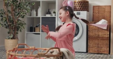 Pembe elbiseli ve örgülü küçük bir kız çamaşırhanenin zemininde oturmuş hasır bir sepetle kıyafetleri düzenliyor, radyodan gelen müzikle dans ediyor..