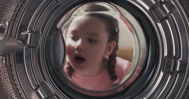 一个震惊的小女孩看着洗衣机里面 她看到一个干净的 有香味的 洗过的鼓 好奇地环顾四周 — 图库视频影像