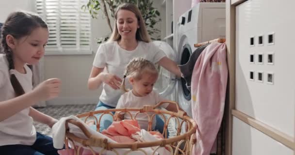 把衣服从柳条筐里拿出来放进洗衣机的鼓里 母亲和孩子们打扫房子 教女儿们打扫 — 图库视频影像