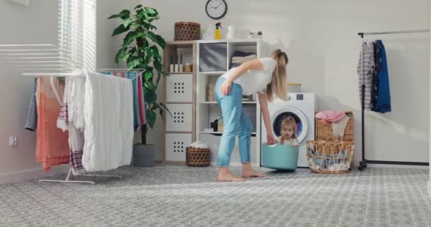 一个快乐的妈妈和她的孩子在洗衣房玩耍 可爱的金发小女孩正坐在衣橱里 女人拉女孩是为了好玩 — 图库视频影像