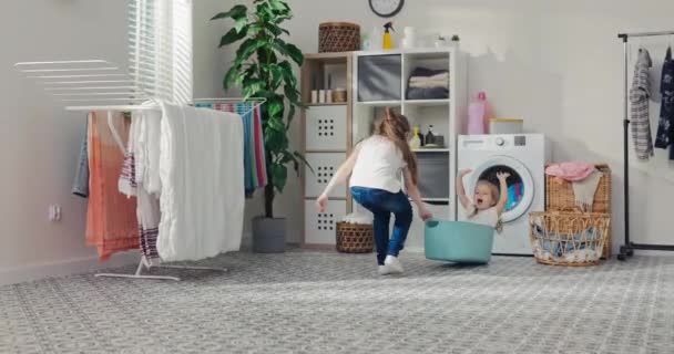 金发蓝眼睛的女孩坐在一个塑料蓝色的衣服碗里 她姐姐在玩她拉着一个婴儿的游戏 这个婴儿高兴地举起双手 尖叫着 玩耍着 — 图库视频影像