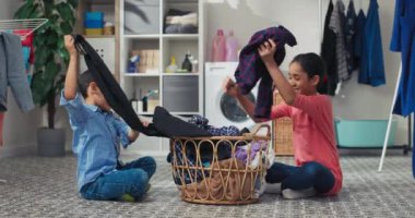 Küçük kız ve erkek kardeş çamaşırları uygun renklerde yıkayıp çamaşır odasında ev işleri yaparak vakit geçiriyorlar..