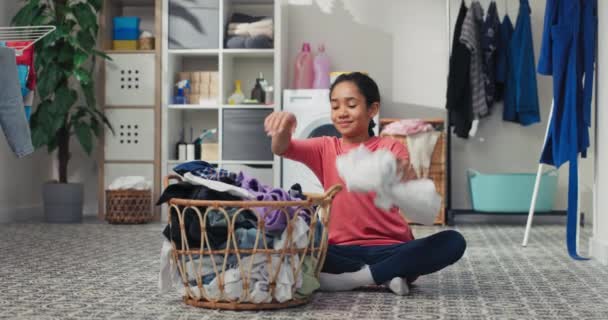 微笑的女孩坐在洗衣房的地板上 面对着一个大柳条筐 手里拿着要整理的衣服 在家务活上花时间 帮助父母 — 图库视频影像