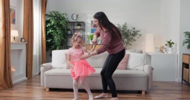 Daughter and mother dancing in modern cozy sunny living room, babysitter and small child enjoy summer day at home, family celebrates vacation, leisure, fun mood, happy active people concept.