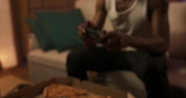 Yorgun bir adam masaya uzanır, odasında vakit geçirir, kanepeye oturur, pizza yer, konsolda oyun oynar..