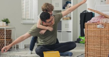 Babam temizlik yaparken oğluyla çamaşır odasında oynuyor. Adam, kollarını açarak bir uçak gibi davranarak çocuğu sırtında tutuyor. Evde çocuklu temizlik kavramı.